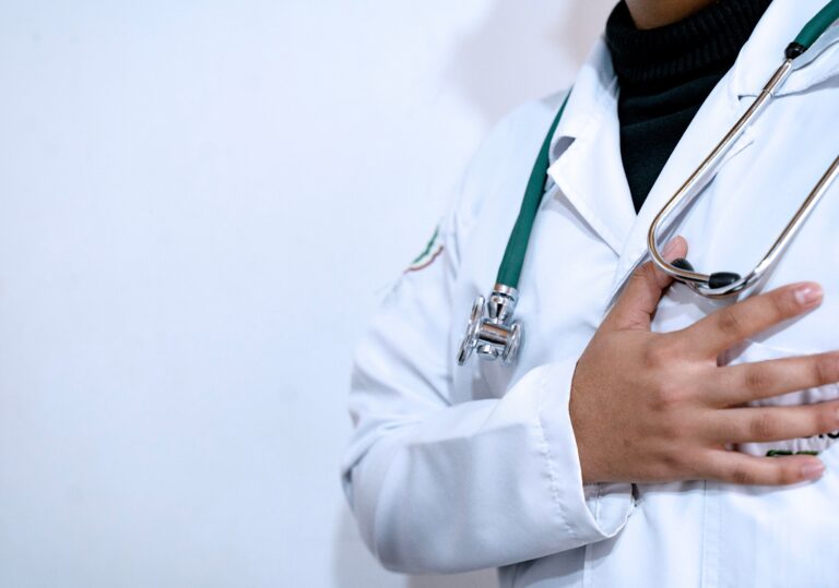 A healthcare professional in a white coat with a stethoscope places a hand over their heart, symbolizing compassion, ethics, and integrity in patient care.