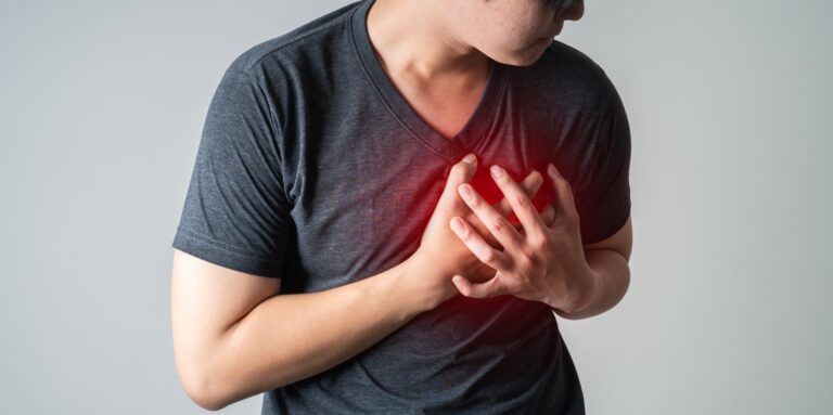 Man clutching his chest in pain with red highlight over the heart area, representing chest pain as one of the critical nursing assessment red flags for possible cardiac emergency.