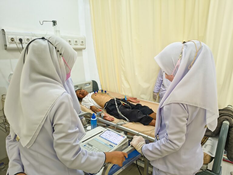 Nurses using a cardiac monitor and stethoscope to assess a male patient lying in a hospital bed, identifying nursing assessment red flags during bedside evaluation and cardiac monitoring.
